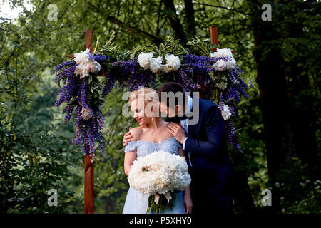 Die Braut und der Bräutigam stand auf der Arch, mit Blumen geschmückt, mit einem großen Blumenstrauß aus den weißen Pfingstrosen. Registrierung vor Ort im Park Hochzeit gehen ein Stockfoto