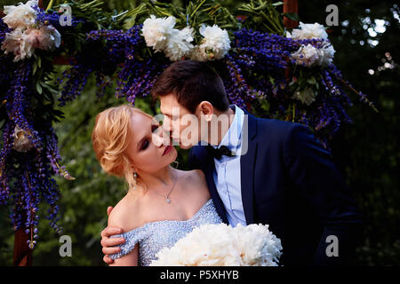 Die Braut und der Bräutigam stand auf der Arch, mit Blumen geschmückt, mit einem großen Blumenstrauß aus den weißen Pfingstrosen. Registrierung vor Ort im Park Hochzeit gehen ein Stockfoto