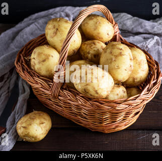 Junge Kartoffeln in einem braunen Weidenkorb auf einem Holztisch Stockfoto