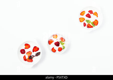 Drei Becher Erdbeereis auf einem weißen Tisch, Ansicht von oben. Flach Zusammensetzung der kalte Desserts mit frischen roten Beeren und Minze und Pu Stockfoto