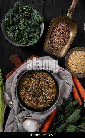 Minestrone mit frischem Spinat, Reis und Linsen, Braun auf schwarz Holz- Hintergrund, Ansicht von oben geschossen. Stockfoto