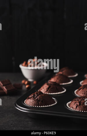 Chocolate muffins Backformen mit Schokolade und die Muttern auf der Seite auf schwarzem Beton vor schwarzem Holz Hintergrund mit kopieren. Stockfoto