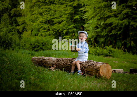 Ein litttle zwei Jahre alte Junge sitzt auf einem Baum und liest ein Buch. hildren Tag. Stockfoto