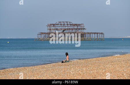 Brighton UK vom 28. Juni 2018 - DE Wetter: Eine junge Frau sitzt allein in der heißen Sonne auf Brighton Beach heute Morgen mit der West Pier im Hintergrund. Das heiße Wetter Prognose in Großbritannien für die nächste Woche mit Temperaturen über 30 Grad in einigen Teilen: Simon Dack/Alamy Live News, um fortzufahren Stockfoto