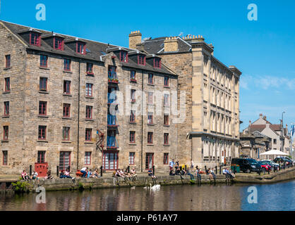 Water of Leith, Edinburgh, Schottland, Großbritannien, 28. Juni 2018. Büroangestellte standen am Flussufer vor dem umgebauten Lagerhaus in Wohnungen namens Cooperage Wohnungen zur Mittagszeit in der heißen Sonne während der Hitzewelle mit Schwäne und Cygnets in der Hoffnung, gefüttert zu werden Stockfoto