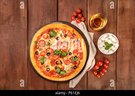 Overhead Foto von Pepperoni Pizza mit Glas Weißwein, Tomaten und Käse mozzarellini, Schuß von oben auf dunklen rustikalen Hintergrund mit Co Stockfoto