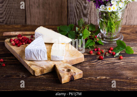 Französischer brie Käse, wilden Erdbeeren und weiß purple Wild Flower Bouquet auf ländlichen Holztisch Stockfoto