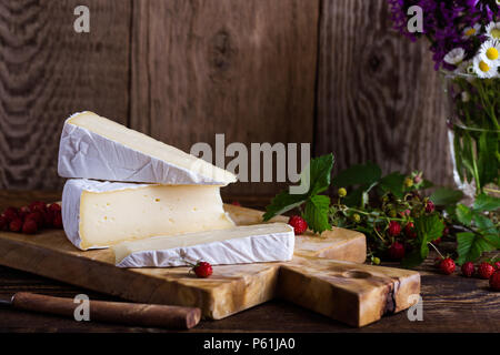 Französischer brie Käse, wilden Erdbeeren und weiß purple Wild Flower Bouquet auf ländlichen Holztisch Stockfoto