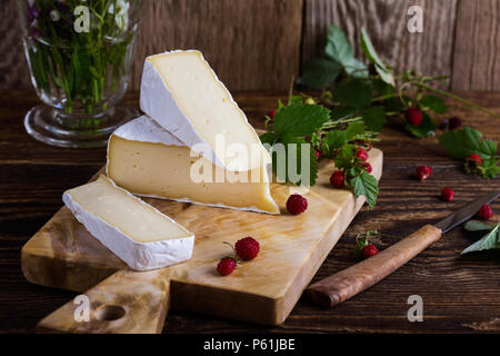 Französischer brie Käse, wilden Erdbeeren und weiß purple Wild Flower Bouquet auf ländlichen Holztisch Stockfoto