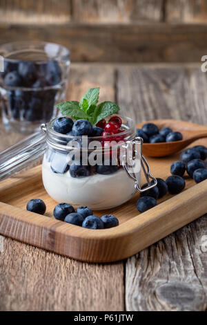 Käsekuchen creme Parfaits mit Heidelbeeren und roten Johannisbeeren Beeren im Glas serviert köstliche Sommer keine-backen Dessert auf rustikalen Holztisch bereit zu essen Stockfoto