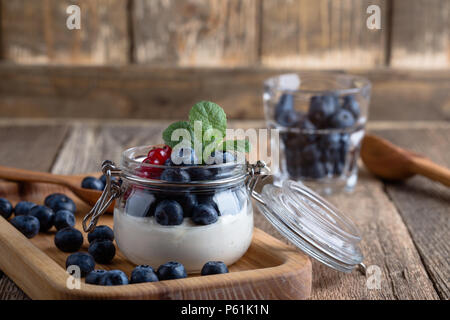 Käsekuchen creme Parfaits mit Heidelbeeren und roten Johannisbeeren Beeren im Glas serviert köstliche Sommer keine-backen Dessert auf rustikalen Holztisch bereit zu essen Stockfoto