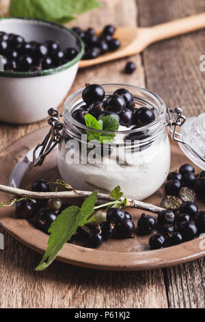 Käsekuchen creme Parfaits mit frischen schwarzen Johannisbeeren in jar, köstliche Sommer keine-backen Dessert auf rustikalen Holztisch bereit zu essen Stockfoto