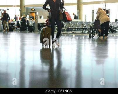 Ein Blick auf die Menschen, mit einem eleganten Frau, die vom Hals abwärts, durch einen Flughafen Terminal mit reflektierenden Etagen, der Stift herausziehen Stockfoto