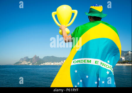 Brasilianischen Fußball-Fan in riesigen Flagge und hat vor der Strand von Ipanema Skyline der Stadt Rio de Janeiro gewickelt. Stockfoto