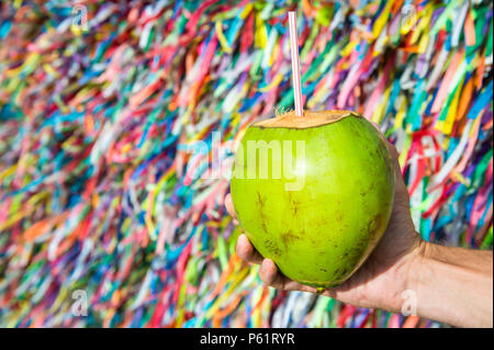 Brasilianische Hand hält Coco Gelado trinken Kokosnuss an Wand des Wunsch Bänder Bonfim Kirche in Salvador Bahia Brasilien Stockfoto