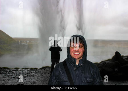 Männliche Touristen stellt sich hinter einem Wasserfall in einen sehr nassen Szene in Eis Stockfoto