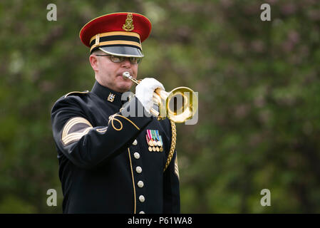 Auf dem Arlington National Cemetery, Abschnitt 30, führte ein Mitglied der U.S. Army Band, bekannt als „Pershing’s Own“, am 25. April 2016 Taps während einer Kranzniederlegung am Grabmal von General John Shalikashvili, ehemaliger Vorsitzender der Joint Chiefs of Staff und Oberster Alliierter Befehlshaber, durch. Die Zeremonie würdigte Shalikaschwilis Militärdienst, Führung und Beiträge zu US-amerikanischen und alliierten Verteidigungsoperationen. Militärangehörige, Würdenträger und Besucher nahmen an zeremoniellen Begebenheiten Teil und erteilten durch formelle militärische Traditionen Respekt. Stockfoto