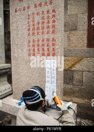 Qingdao, China - Dezember 2017: älterer Mann carving Namen und Spende auf s im Taiqing Tempel Stele, Laoshan Stockfoto