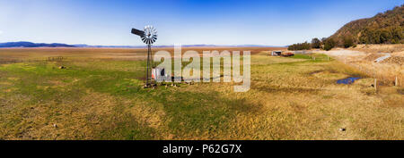 Flache Ebene von Dry Lake George in NSW und Akt der Australien Open mit Rinder Farm und remote einzelne Mühle gegen den blauen Himmel. Stockfoto