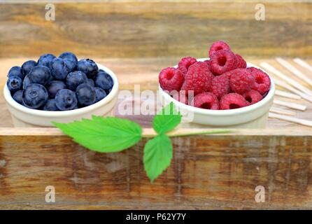 Gesunde Lebensmittel, Landwirtschaft, Ernte und Früchte Konzept: frische reife Heidelbeeren und Himbeeren in zwei Schalen auf einem hölzernen Fach. Stockfoto