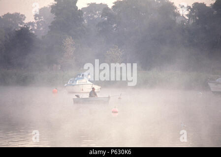 Einsame Mann, um die Fischerei mit kleinen Beiboot in der Morgendämmerung, Oulton Broad, Suffolk, England, 1975 Stockfoto