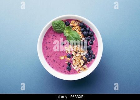 Smoothie Schüssel mit Müsli, Blaubeeren und Minze auf blauem Hintergrund. Gesundes Frühstück, Ansicht von oben. Stockfoto