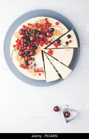 Hausgemachter Käsekuchen New York mit Beeren auf weiße Holztisch. Ansicht von oben. Rote Johannisbeere, schwarze Johannisbeere und Kirsche. Stockfoto