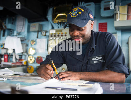 Ein Quartermaster 2nd Class stellt am 15. April 2016 Navigationspositionen auf einer Karte im Pilothaus an Bord der USS Whidbey Island (LSD 41) im Atlantik dar. Das Schiff arbeitet mit der Wasp Amphibious Ready Group während einer ARG/MEU-Übung. Zu den Operationen gehören Navigation, Seemannschaft, Brückenüberwachung, Kommunikation, Koordination, und Sicherheitsbohrer. Die Crew-Mitglieder führen Diagrammaufzeichnungen, Kursanpassungen und Überwachung durch, um die Einsatzbereitschaft zu gewährleisten und die Ziele der amphibischen Mission zu unterstützen. Stockfoto