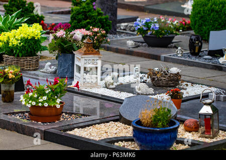 Grabsteine auf einem Friedhof mit vielen verschiedenen Blumen. Stockfoto