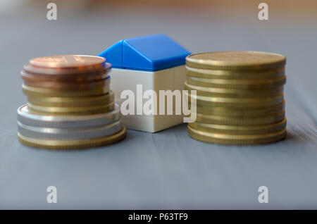 Das Konzept der Kredite für den Wohnungsbau. Weißes Haus mit blauen Dach auf einem Stapel von Münzen Stockfoto