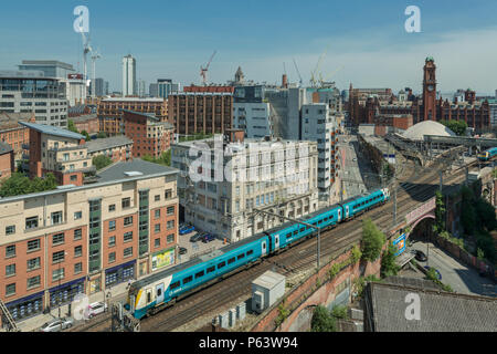 Ein Arriva Zug kommt an Bahnhof Oxford Road in Manchester, mit der Skyline der Stadt im Hintergrund. Stockfoto