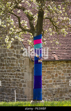 Garn Bombenanschlag oder yarnbombing: Ein blühender Baum mit bunten stricken Dekoration. Stockfoto