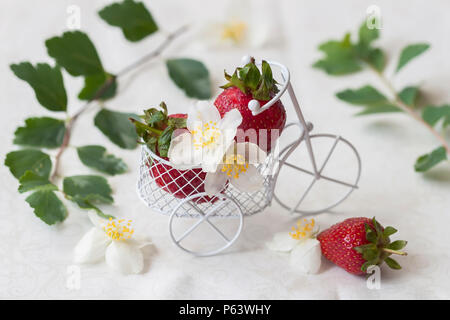 Miniatur Spielzeug Warenkorb, Trolley closeup mit reifen Erdbeeren, Blätter, Blumen auf hellem Hintergrund. Konzept der gesunden Ernährung, Entgiftung, Vitamine, Diät Stockfoto