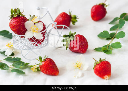 Miniatur Spielzeug Warenkorb, Trolley mit reifen Erdbeeren, Blätter, Blumen auf hellem Hintergrund. Vegetarische Konzept, Ernährung, Entgiftung, organische Vitamine Stockfoto