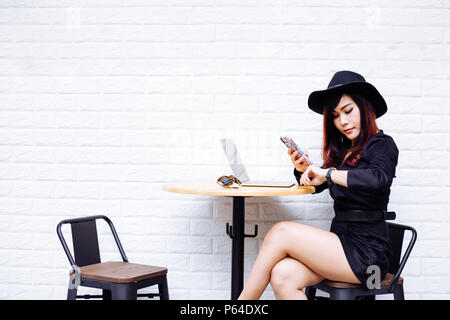 Junge modische Asian Business Frau an Watch suchen, warten, dass jemand mit einem Handy und Laptop. Zu spät zum Termin Konzept Stockfoto