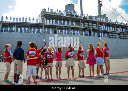 SANTA Rita, Guam (11. April 2016) - Studenten der McCool Grundschule durchführen Chor wave Flags auf Sierra Pier gastfreundliches Haus Matrosen an Bord der U-Boot Tender USS Emory S. Land (39), April 11. Die Rückkehr nach Guam ist Emory S. Land's erste seit dem Wechsel von homeport von Diego Garcia nach Guam, Dez. 23. Emory S. Land ist ein EXPEDITIONARY U-Boot Ausschreibung Durchführung von koordinierten neigten, Liegeplätze und flott Wartung in den USA 5. und 7 Flotten Bereiche. (U.S. Marine Foto von Massenkommunikation Seaman Apprentice Alana Langdon/Freigegeben) Stockfoto