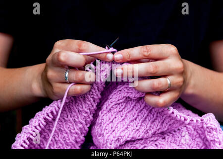 Close-up junge Frau in schwarzen T-Shirt strickt mit Stricknadeln lilic Pullover aus natürlichen Wollfäden Stockfoto