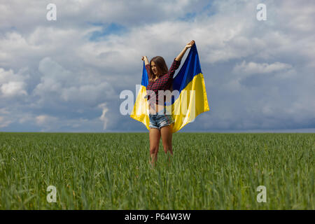 Junge schöne ukrainische Mädchen mit eine ausgezeichnete Figur in kurze Jeans Shorts hält einen Nationalen Ukrainischen gelb Blaue Flagge im Wind wieder Stockfoto