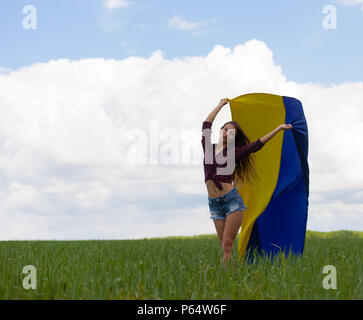 Junge schöne ukrainische Mädchen mit eine ausgezeichnete Figur in kurze Jeans Shorts hält einen Nationalen Ukrainischen gelb Blaue Flagge im Wind wieder Stockfoto