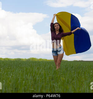 Junge schöne ukrainische Mädchen mit eine ausgezeichnete Figur in kurze Jeans Shorts hält einen Nationalen Ukrainischen gelb Blaue Flagge im Wind wieder Stockfoto