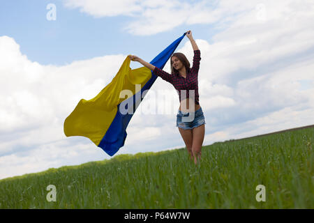 Junge schöne ukrainische Mädchen mit eine ausgezeichnete Figur in kurze Jeans Shorts hält einen Nationalen Ukrainischen gelb Blaue Flagge im Wind wieder Stockfoto