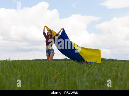 Junge schöne ukrainische Mädchen mit eine ausgezeichnete Figur in kurze Jeans Shorts hält einen Nationalen Ukrainischen gelb Blaue Flagge im Wind wieder Stockfoto