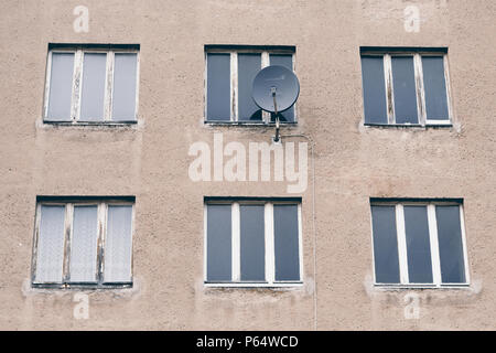 Ein hellbraunes herunter kommenes Nebengebäude mit verschimmelten Fensterrahmen und Parabolantenne bei der Prora auf Rügen in Deutschland. Stockfoto