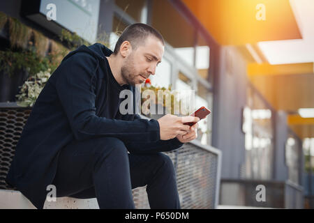 Bärtiger Mann sitzt auf einem Schritt und Mobiltelefon. Stockfoto