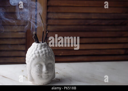 Buddha Kopf mit Weihrauch auf Holz und Marmor Hintergrund Stockfoto