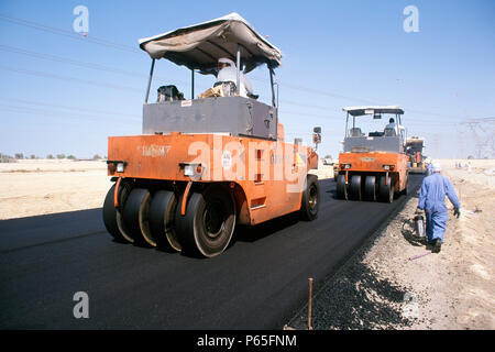Ein Trupp von müde Rollen besteht, ist für den Abschluss der Arbeiten auf dem Asphalt Oberfläche eines slip Road, Dubai, UAE verwendet. Stockfoto