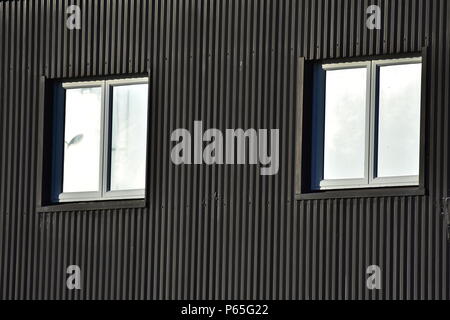 Zwei Fenster auf dunklen Außenwand aus Wellblech. Stockfoto