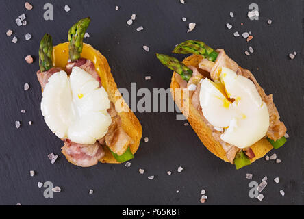 Gegrillte Toast mit Spargel in Schinken und pochiertem Ei auf hölzernen Hintergrund Stockfoto