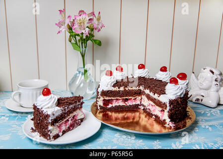 Schokoladenkuchen mit Sahne und Kirsche auf dem Serviertisch. Stockfoto