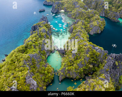 Antenne drone Blick auf hölzerne Boote und Kajaks in einem schönen flachen tropischen Lagune umgeben von zerklüfteten Klippen (kleine und große Lagune, El Nido) Stockfoto